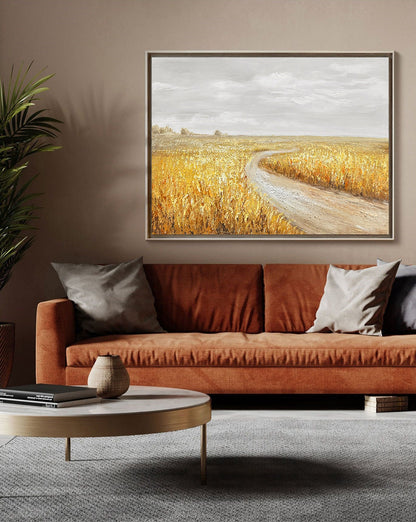 May include: A painting of a winding dirt road leading through a field of golden wheat. The sky is a light gray with a few clouds. The painting is framed in a simple, gold frame.