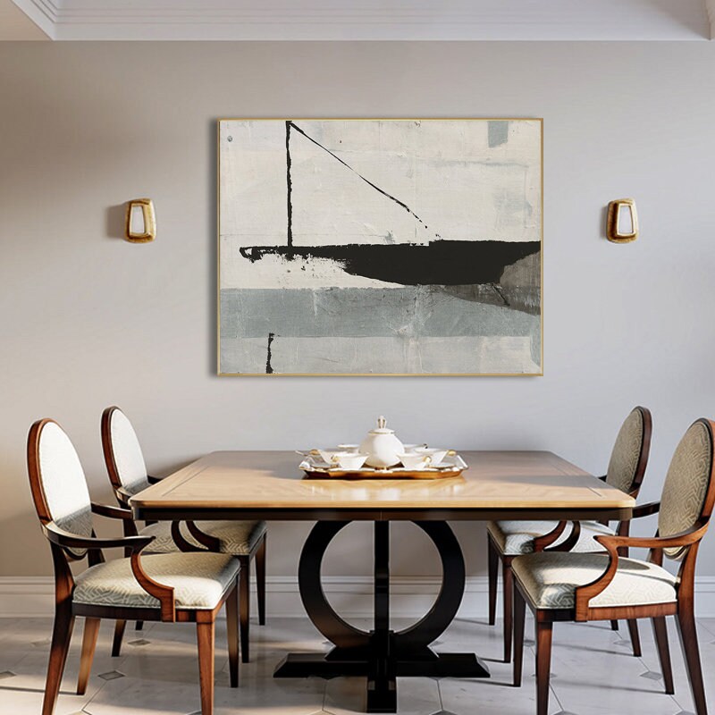 May include: A black and white abstract painting with a gold frame hangs above a wooden dining table with four chairs. The painting features a large black shape with a diagonal line.