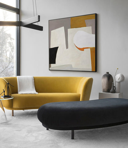 May include: A mustard yellow velvet sofa with a white throw blanket sits in front of a large abstract painting with geometric shapes in shades of gray, white, orange, and brown. A black oval ottoman sits in front of the sofa.