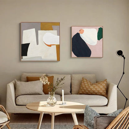 May include: Two abstract paintings in square frames, one with white, gray, black, and orange shapes, the other with white, pink, green, and blue shapes, hanging on a beige wall above a light beige sofa with two pillows.
