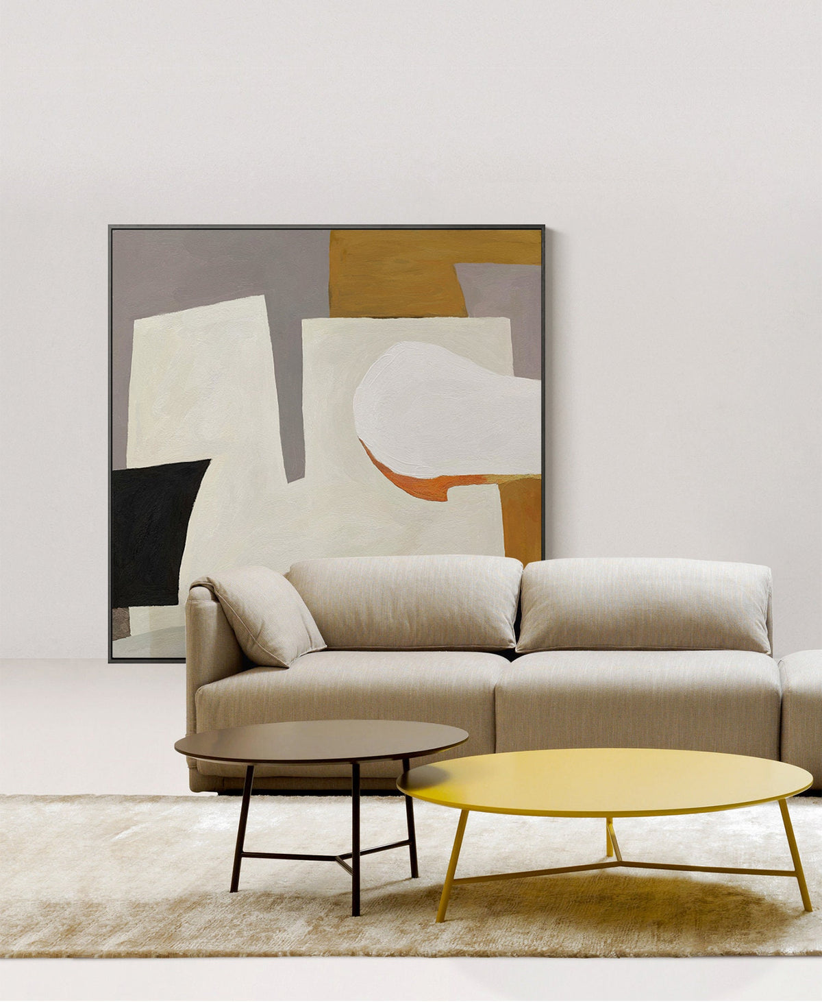 May include: A beige sectional sofa with two coffee tables, one brown and one yellow, in front of a framed abstract painting with white, gray, black, and orange shapes.