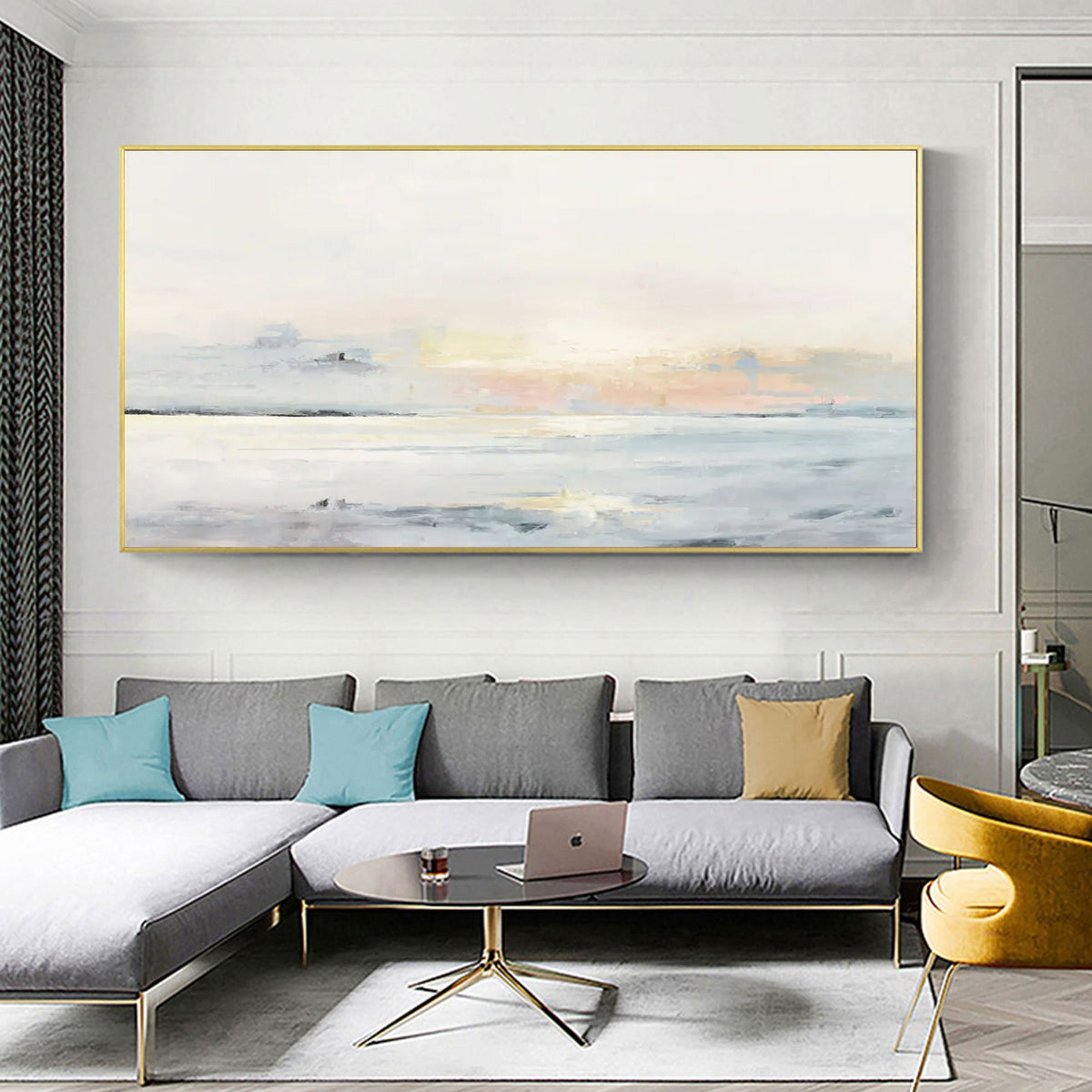 May include: A large rectangular abstract painting with a gold frame. The artwork depicts a seascape with soft pastel colors of white, blue, and peach. The painting hangs above a gray sectional sofa with blue and gold throw pillows.