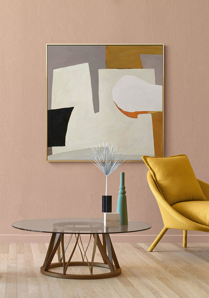 May include: Abstract art painting with geometric shapes in shades of white, gray, black, orange, and brown. The painting is framed in gold and hangs on a light pink wall above a glass coffee table with a wooden base.