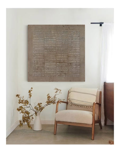 May include: A square wall art piece featuring a textured, taupe-colored surface with a repeating horizontal line pattern. The artwork is mounted on a plain wall above a wooden armchair with a cream-colored cushion and a striped throw blanket.