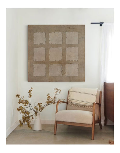 May include: A beige armchair with a white and black striped throw blanket sits in a room with a large abstract painting on the wall. The painting is a light brown color with a grid of squares.