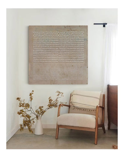 May include: A beige armchair with a white and black striped throw blanket sits in a room with a large abstract painting on the wall. The painting features a pattern of small white circles on a beige background.