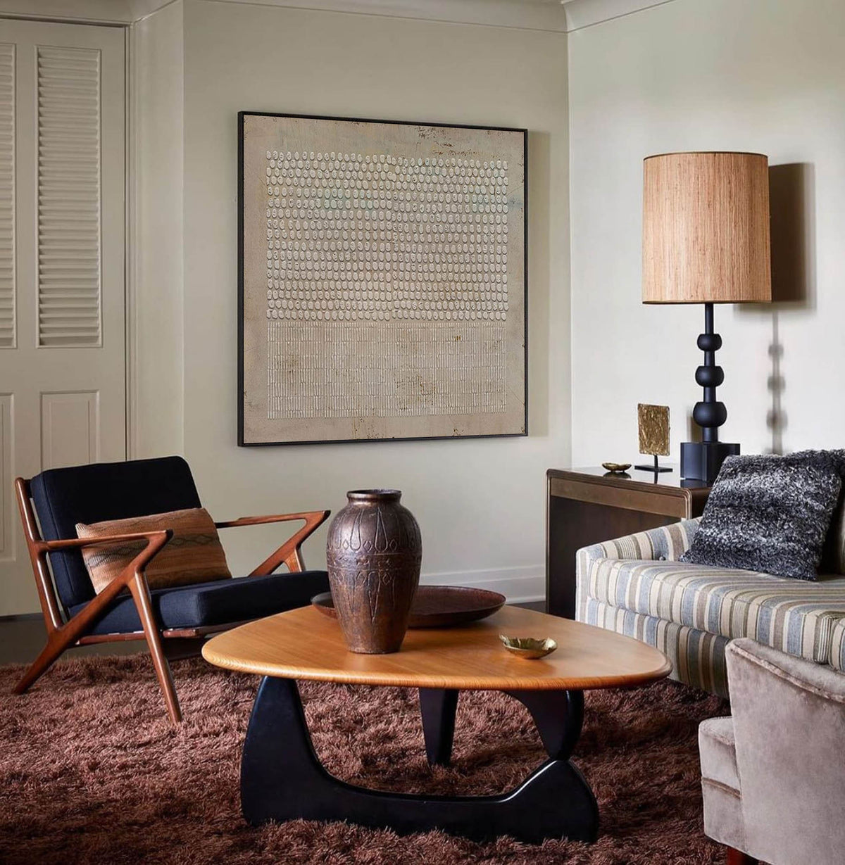 May include: A mid-century modern living room with a brown leather armchair, a coffee table with a wood top and black legs, a brown ceramic vase, and a couch with a striped fabric and a black and white throw pillow.