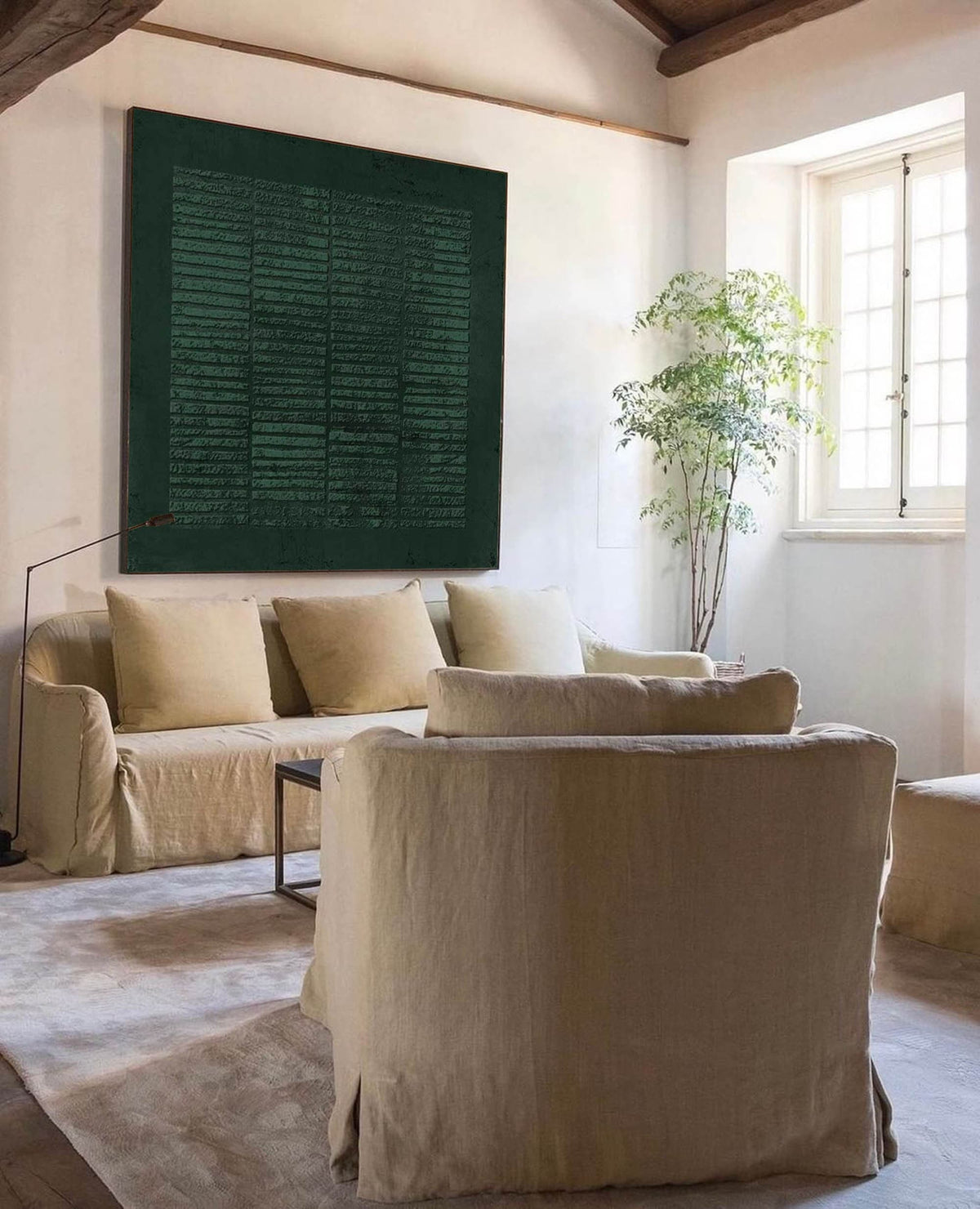 May include: A living room with a large green abstract painting on the wall, a beige sofa with pillows, and a beige armchair. The room has a wooden beam ceiling and a large window with white blinds.