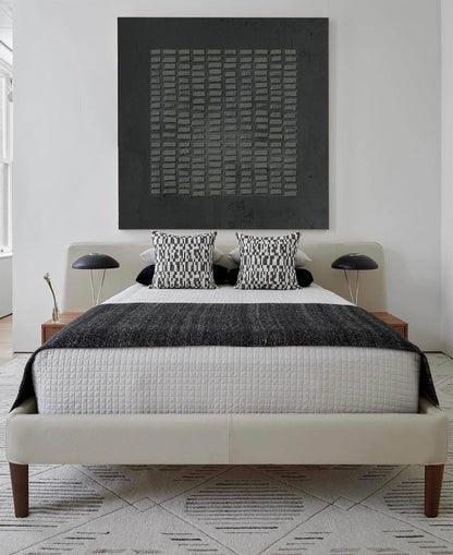 May include: A bed with a cream-colored upholstered frame and wooden legs, featuring a white quilted coverlet, a dark gray textured throw blanket, and two black and white patterned square pillows. Two black dome-shaped lamps sit on wooden nightstands.