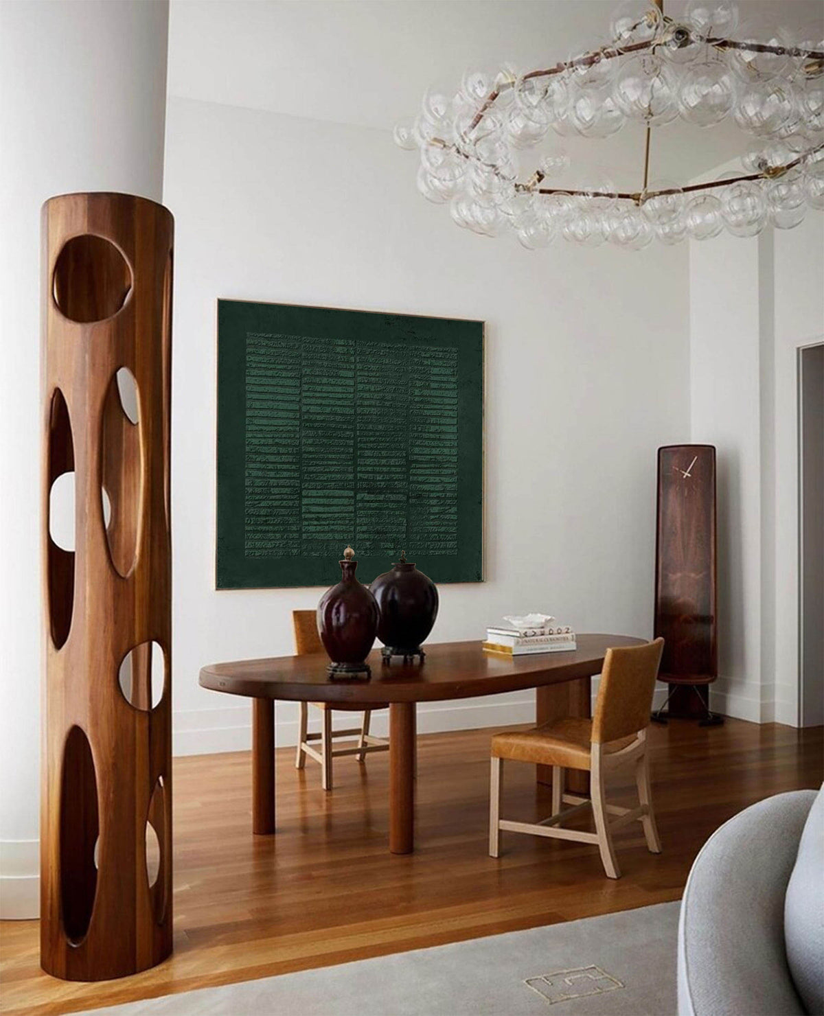 May include: A modern dining room with a wooden table and chairs, a large green abstract painting on the wall, and a unique wooden sculpture with cutouts. A chandelier with clear glass globes hangs from the ceiling.
