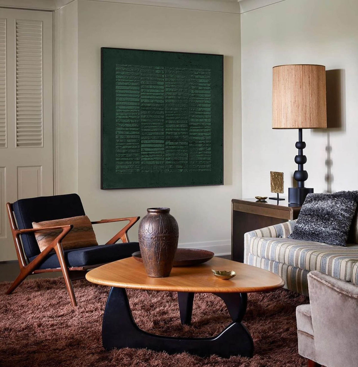 May include: A mid-century modern living room with a brown leather armchair, a striped sofa, a brown ceramic vase, a coffee table with a wood top and black legs, and a lamp with a woven shade.
