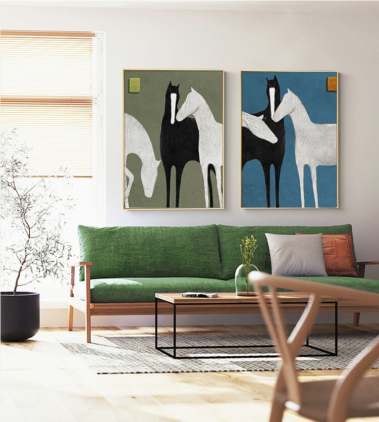 May include: Two abstract paintings of horses in a minimalist style. The paintings are framed and hung on a wall above a green sofa. The painting on the left has a green background and the painting on the right has a blue background.