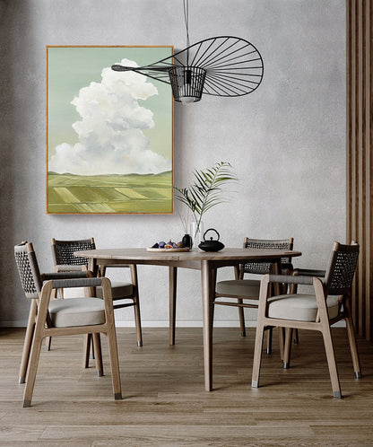 May include: A dining room with a wooden table and chairs. The table is set with a bowl of fruit and a teapot. A painting of a cloudy sky and green fields hangs on the wall above the table. A black metal light fixture hangs from the ceiling.