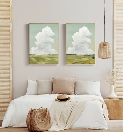 May include: Two framed landscape paintings with a green field and a white cloud in the sky. The paintings are hanging on a light gray wall above a white bed with a white blanket and a brown woven basket.