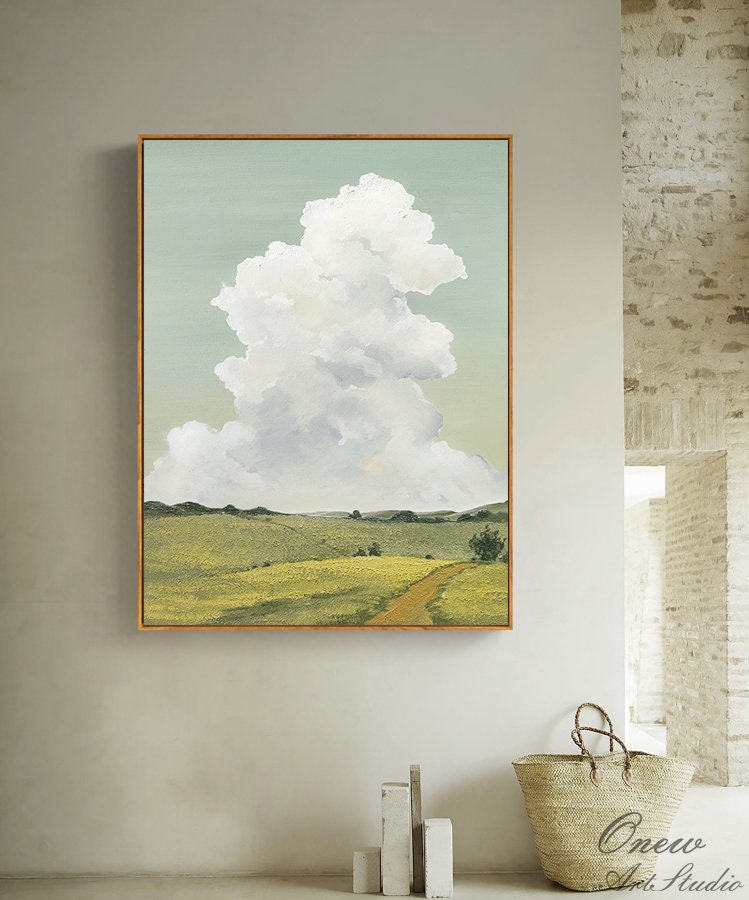 May include: A painting of a landscape with a large white cloud in the sky. The landscape is a field of green grass with a dirt road leading through it. The painting is framed in a light wood frame.