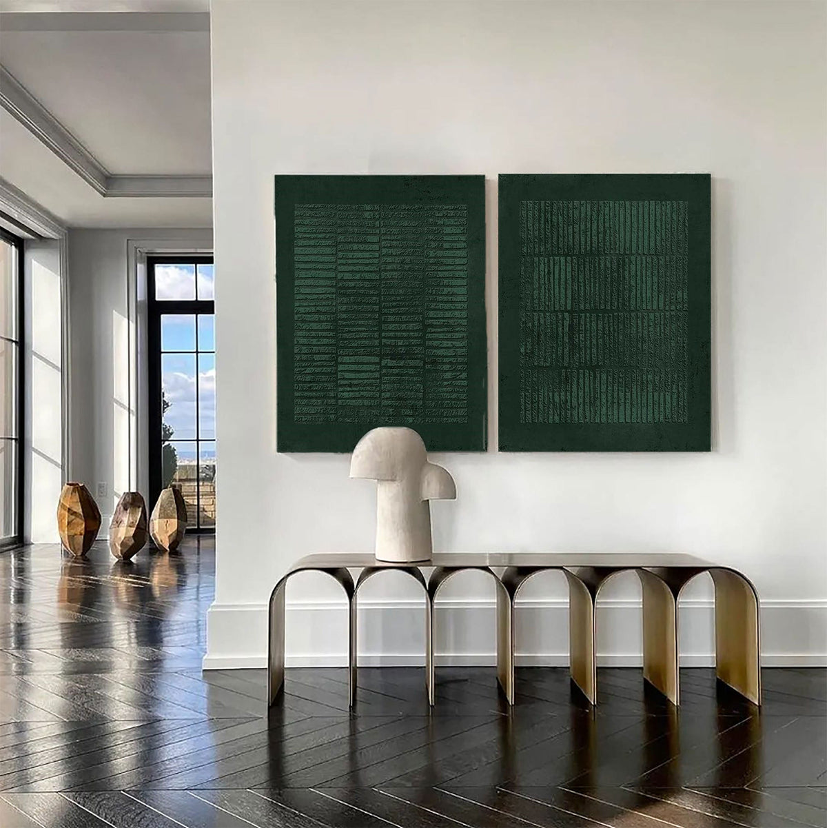 May include: Two rectangular dark green textured wall art pieces hang side by side above a metallic gold console table with arched legs. A beige sculptural lamp sits on the table. The artwork features repeating horizontal and vertical line patterns.