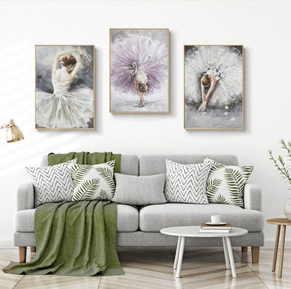 May include: Three framed paintings of ballerinas in various poses. The ballerinas are wearing white and purple tutus. The paintings are hung on a white wall above a gray couch with green throw pillows.