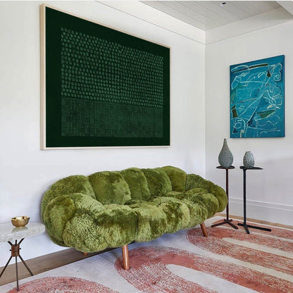 May include: A moss green, textured, fluffy sofa with a tufted design and wooden legs. Above it hangs a large, dark green rectangular artwork featuring a grid of dots and vertical lines, alongside a smaller blue abstract painting on the wall.