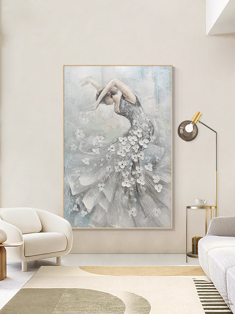 May include: An abstract painting of a dancer in a flowing gown. The artwork features a woman in a silver dress adorned with white floral accents. The background is a soft blend of gray and blue hues, framed in a light wood.