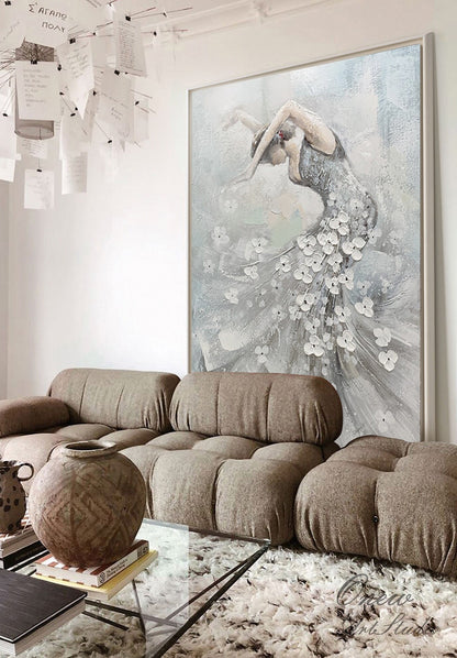 May include: Large framed painting of a dancer in a flowing gown, with white floral accents. The artwork features a muted color palette of gray, white, and pale blue. The painting is displayed above a brown sectional sofa and a glass coffee table.