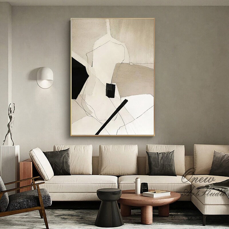 May include: Abstract painting with geometric shapes in black, white, and beige colors. The painting is framed in a gold frame and hangs on a wall in a living room setting.