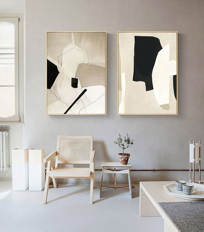 May include: Two abstract paintings with a beige background and black and white geometric shapes. The paintings are framed in gold and hung on a light gray wall.