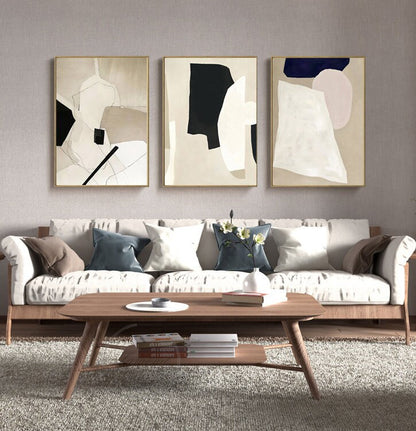May include: Three abstract art prints with geometric shapes in black, white, beige, and pink. The prints are framed in gold and hung on a light gray wall above a white sofa with pillows.