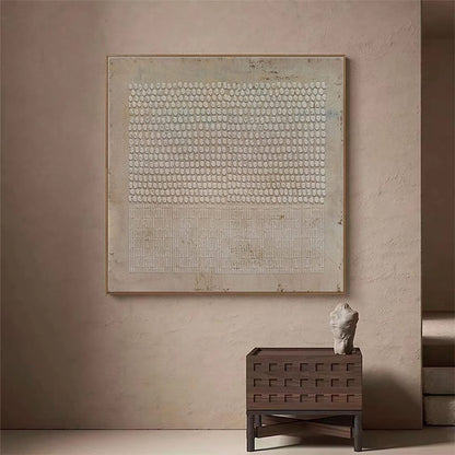 May include: A framed abstract painting with a white and gray pattern of circles and lines. The painting is hanging on a light beige wall above a wooden side table with a small white sculpture on top.