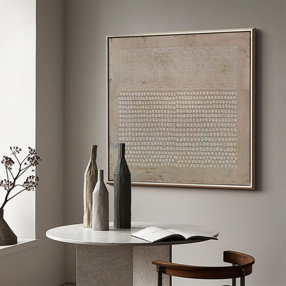 May include: A square framed wall art piece featuring a beige textured background with a top section of vertical white lines and a bottom section of repeating white oval shapes. The artwork is displayed in a thin metallic frame on a neutral wall.