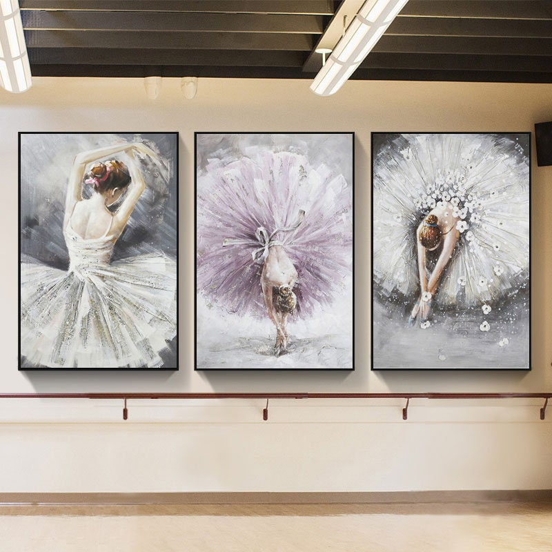 May include: Three framed paintings of ballerinas in various poses. The ballerinas are wearing white and purple tutus. The background of the paintings is a light gray.