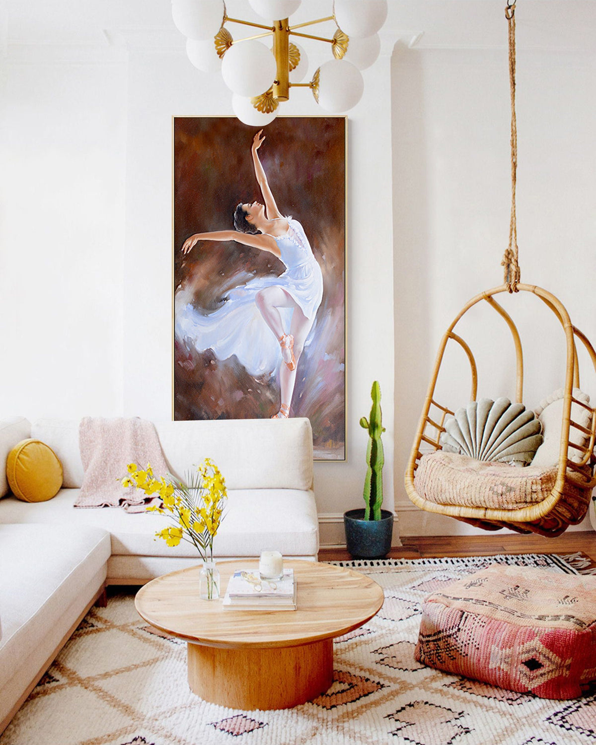 May include: A white couch with a yellow throw pillow sits in a living room with a white rug. A wooden coffee table with a vase of yellow flowers and a book sits in front of the couch. A hanging wicker chair with a light green pillow hangs from the ceiling. A painting of a ballerina in a white dress hangs on the wall above the couch. A cactus plant sits in a blue pot on the floor.