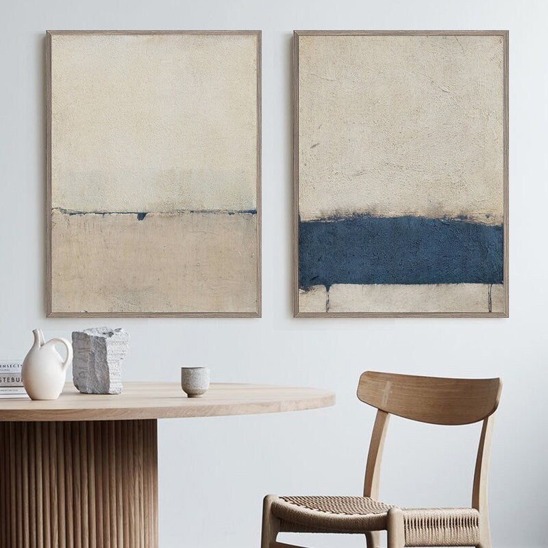 May include: Two abstract paintings in simple frames, one with a light beige background and a thin blue line, the other with a light beige background and a thick blue band.