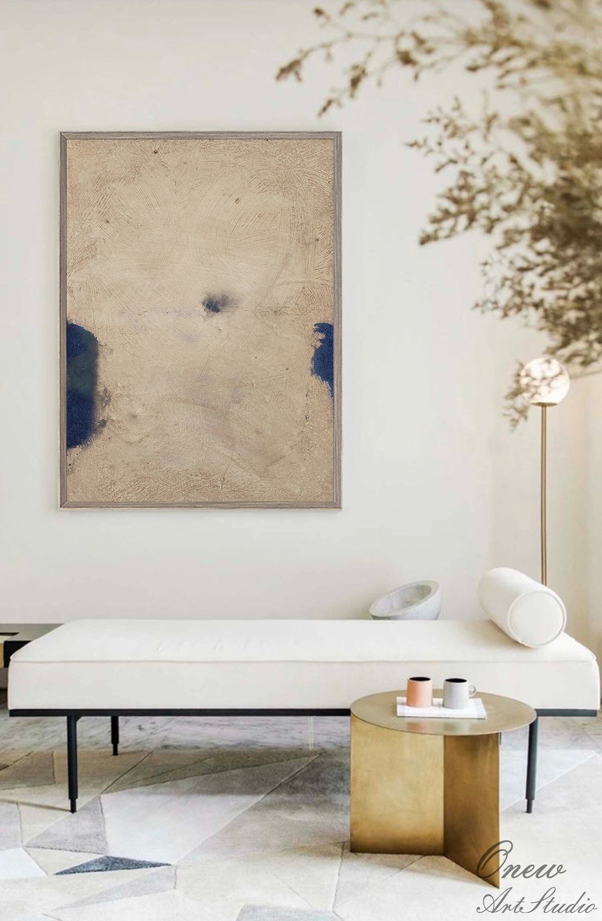 May include: A white bench with a black metal frame and a white pillow. A gold side table with three cups on a white plate. The bench and table are on a white and gray patterned rug. A framed abstract painting with blue and beige colors hangs on the wall.
