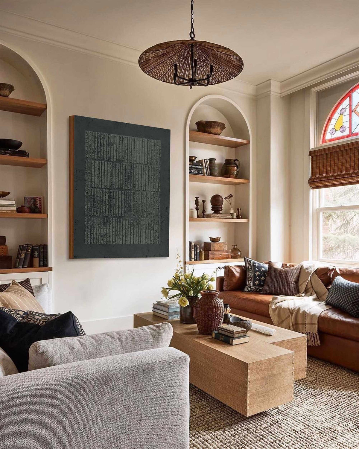 May include: A living room with a large abstract artwork, a brown leather sofa, and a light-colored sofa. A wooden coffee table sits in front of the sofa, and a woven chandelier hangs from the ceiling. Shelves are built into the wall.