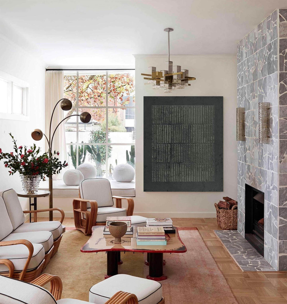 May include: A modern living room with a neutral color palette. Features include a gray fireplace, a large abstract painting, a red-trimmed coffee table, and a stylish chandelier. The room is furnished with light-colored sofas and chairs.