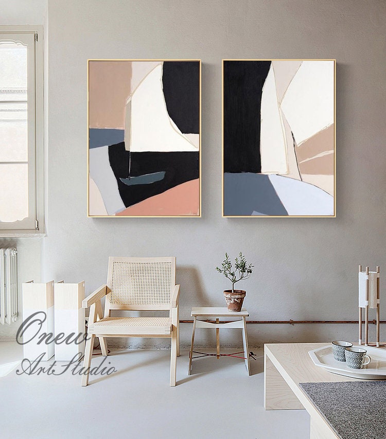 May include: Two abstract paintings with geometric shapes in shades of brown, black, white, and blue. The paintings are framed in gold and hung on a light gray wall.