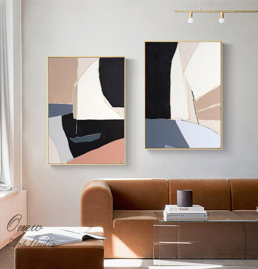 May include: Two abstract paintings with geometric shapes in shades of brown, white, black, and blue. The paintings are framed in gold and hung on a white wall.