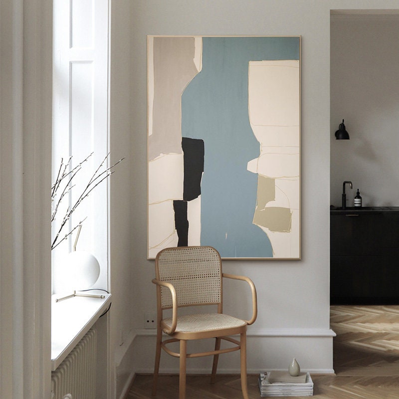 May include: Abstract art painting with geometric shapes in shades of beige, black, white, and blue. The painting is hanging on a white wall in a room with a wooden chair and a window.