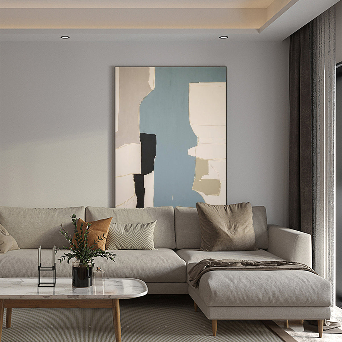 May include: A light gray sectional sofa with a brown throw blanket and pillows. The sofa is in front of a light gray wall with an abstract painting in a black frame.