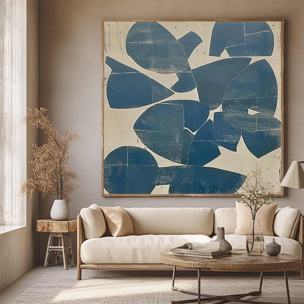 May include: Large abstract painting with a wooden frame. The artwork features navy blue shapes on a cream background. The painting hangs above a cream-colored sofa with wooden legs, a round coffee table, and a side table.