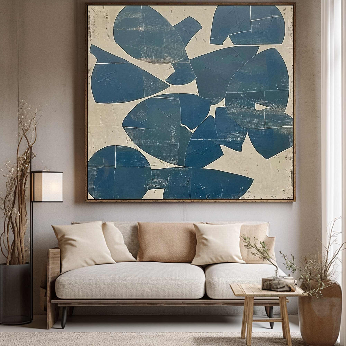 May include: Abstract wall art featuring a large, square canvas with a wooden frame. The artwork displays a pattern of overlapping blue shapes against a cream-colored background. The painting hangs above a light-colored sofa with neutral-toned pillows.