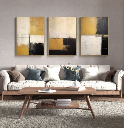 May include: Three abstract paintings in gold, white, and black frames. The paintings are in a minimalist style with geometric shapes and muted colors. The paintings are hung on a light gray wall above a white sofa with pillows.