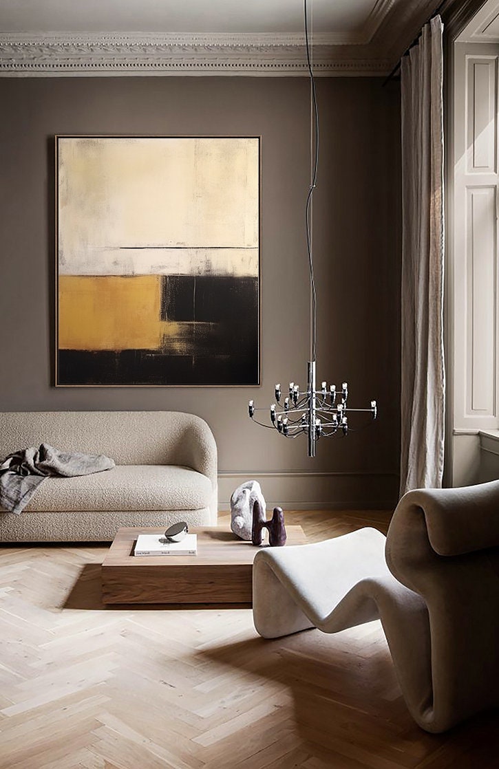 May include: A modern living room interior with a beige sofa, a white armchair, a wooden coffee table, and a large abstract painting in gold, black, and white on the wall. A chrome chandelier hangs from the ceiling.