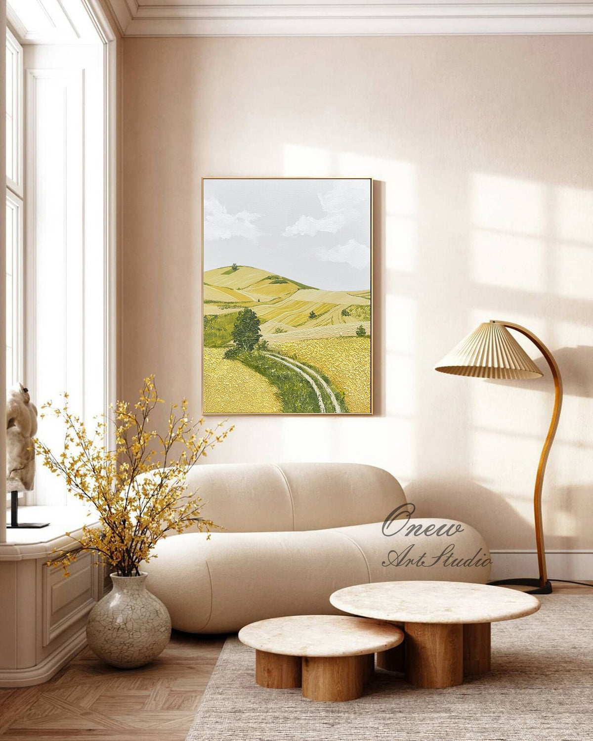 May include: A painting of a landscape with rolling hills, a dirt road, and a single tree in the foreground. The sky is a light blue with white clouds. The painting is framed in a gold frame and hanging on a wall in a living room.