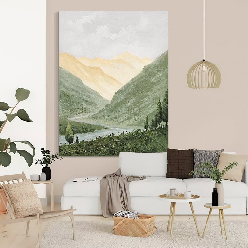 May include: A painting of a mountain landscape with a river winding through the valley. The mountains are painted in shades of green and yellow, with a light blue sky above. The painting is framed and hanging on a wall in a living room.