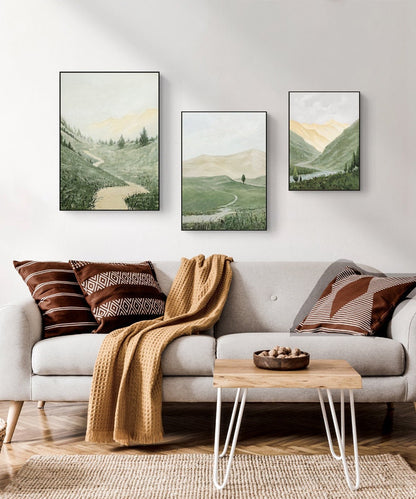 May include: Three framed landscape paintings of green hills and valleys with a winding path. The paintings are hung on a white wall above a light gray sofa with brown and white striped throw pillows and a brown throw blanket.