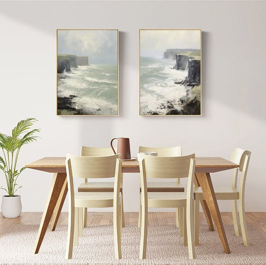 May include: Two framed paintings of a seascape with cliffs and crashing waves. The paintings are hanging on a white wall above a wooden dining table with six chairs.