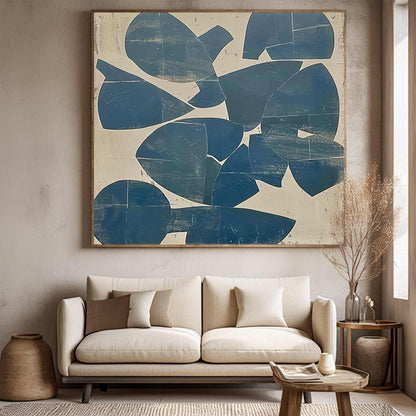 May include: Large abstract painting with a wooden frame. The artwork features overlapping blue shapes on a beige background. The painting hangs above a beige sofa with decorative pillows, creating a modern living room aesthetic.