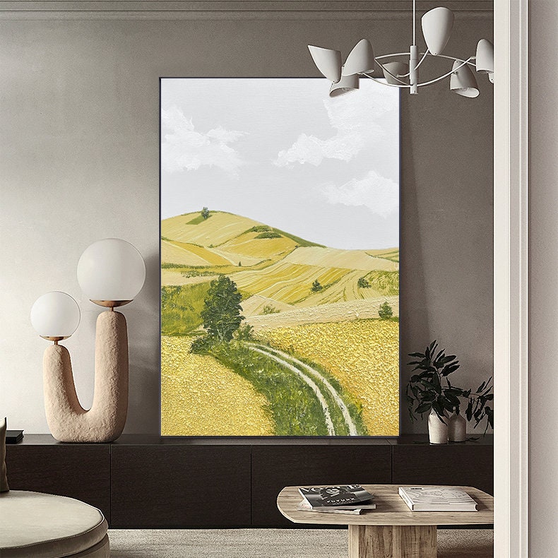 May include: A painting of a rural landscape with rolling hills, a dirt road winding through a field of yellow wheat, and a single tree in the foreground. The sky is a light blue with white clouds.