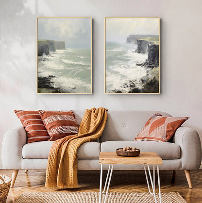 May include: Two framed paintings of a seascape with cliffs and crashing waves. The paintings are hung on a white wall above a gray couch with brown and white throw pillows and a brown blanket.